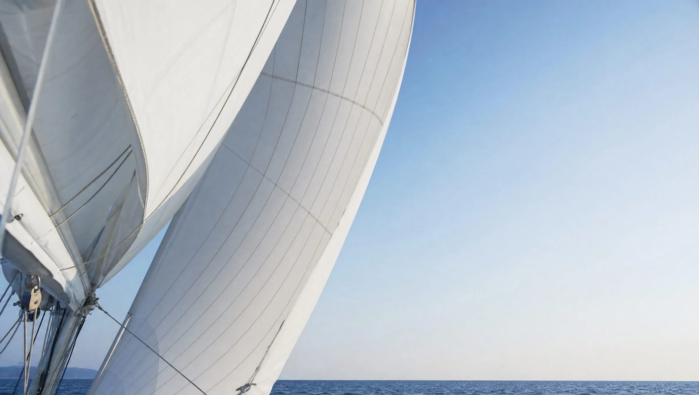 A white sail filled by the wind against a pale morning sky